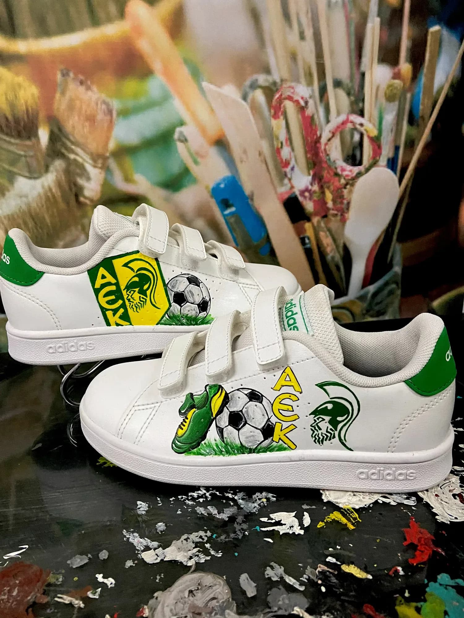 Λευκά παιδικά sneakers με velcro και ζωγραφισμένο έμβλημα της ΑΕΚ, μπάλα και ποδοσφαιρικό παπούτσι
