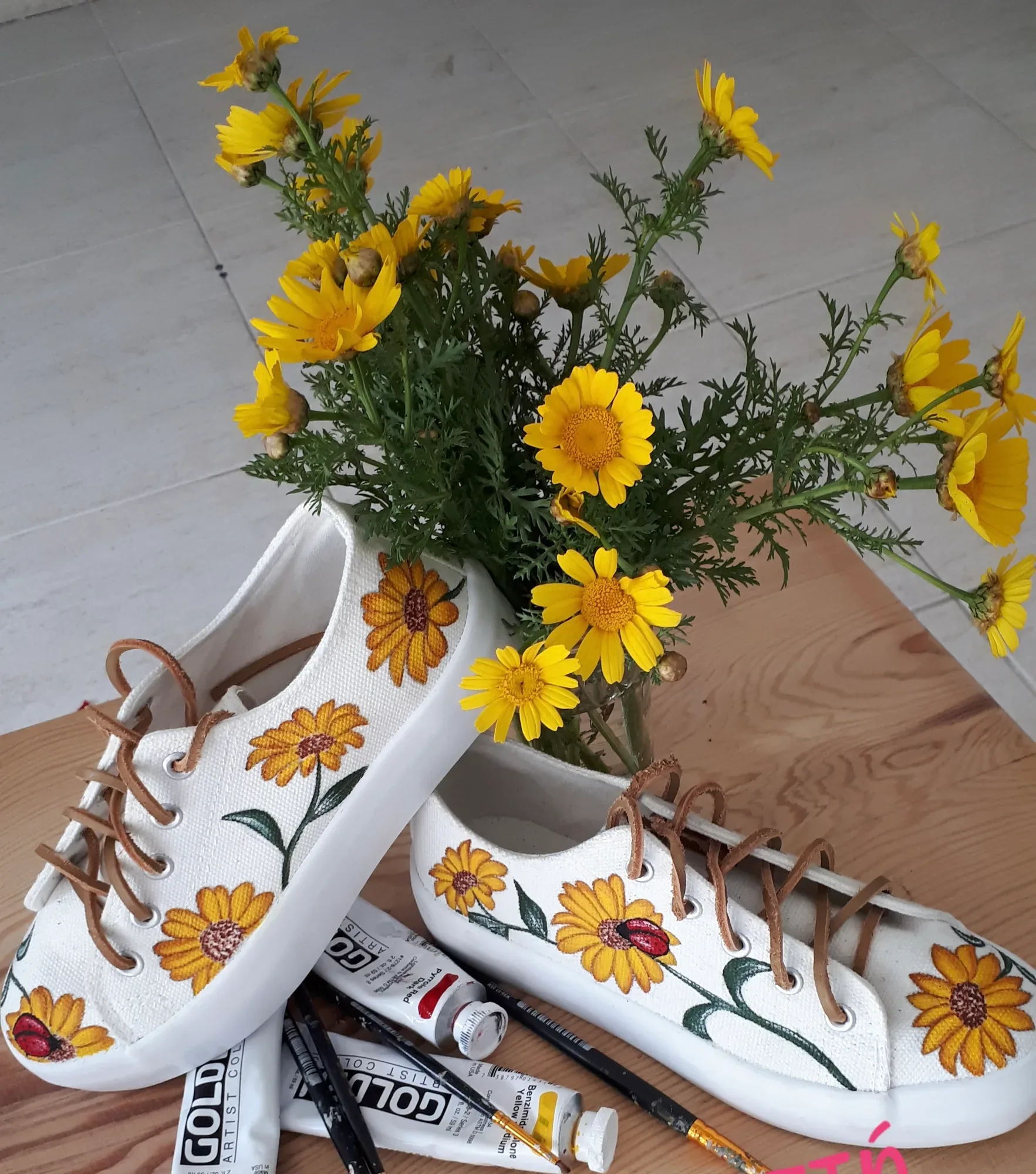 Λευκά sneakers με ζωγραφισμένα ηλιοτρόπια δίπλα σε φρέσκα λουλούδια